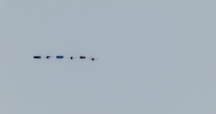 Three people ski across an arctic landscape pulling pulkas