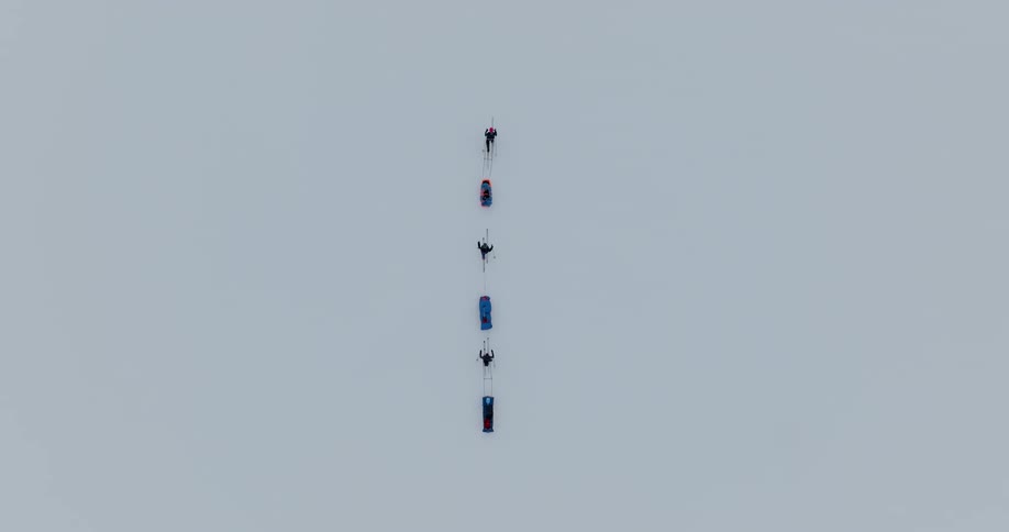 Skiers pulling sleds move slowly across snow