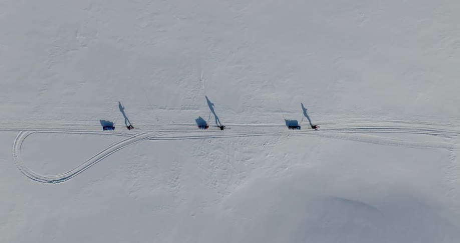 An aerial straight down view of three hikers walking through the snow dragging sleds behind them