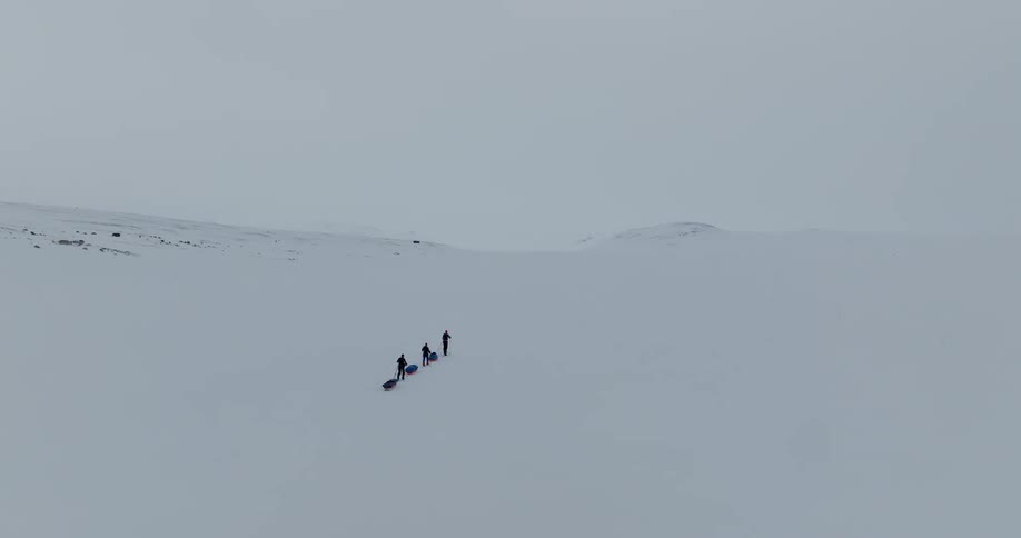 A group of people trek through the snow while pulling sleds in single file
