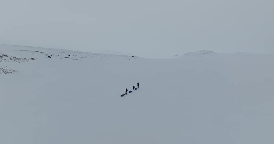 Three people moving through an arctic landscape pulling pulkas behind them