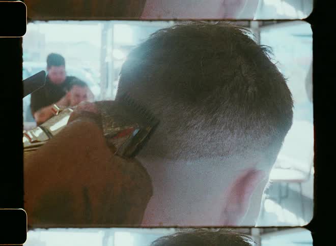 A barber uses an electric razor to buzzcut the hair on the back of a mans head