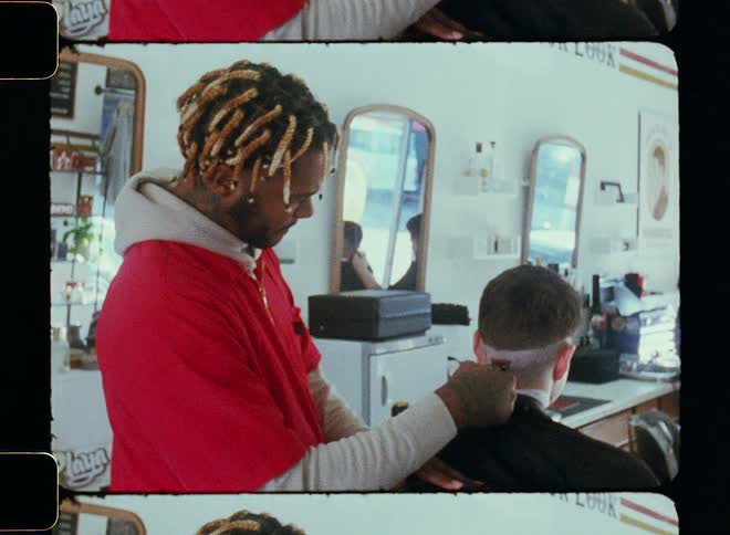 A barber trimming a customers hair sitting in the chair in front of him