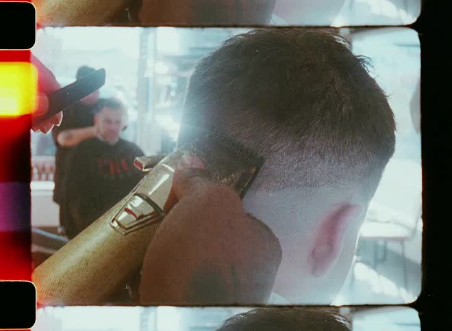 Man getting a fade at a barbershop with another person next to him also getting a trim