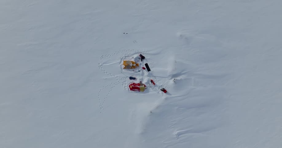An aerial straight down shot of people set up for camp on a snow covered ground