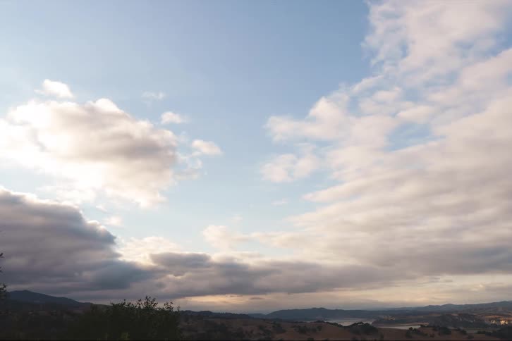 Clouds move over a rural hillside with mountains on the horizon