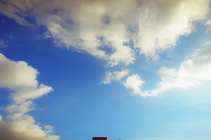 The sun shines on cumulus clouds as they move across a blue sky