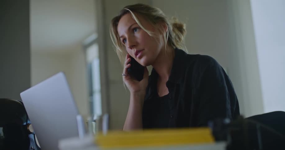 A young woman is talking on the phone and is using her laptop