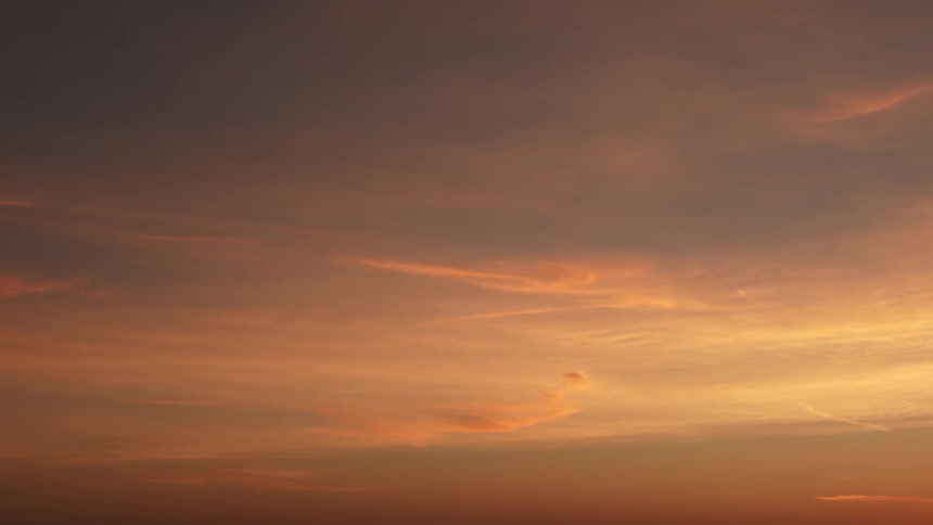 The thick clouds in the sky turn yellow and orange as the sun sets
