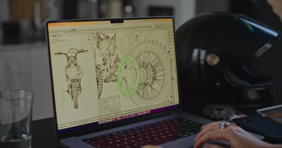 Person working at desk with crash helmet on it manipulates cad cam drawing of gear on a motorcycle