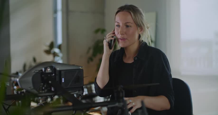 Woman sitting at a desk talks on the phone while working on a drone
