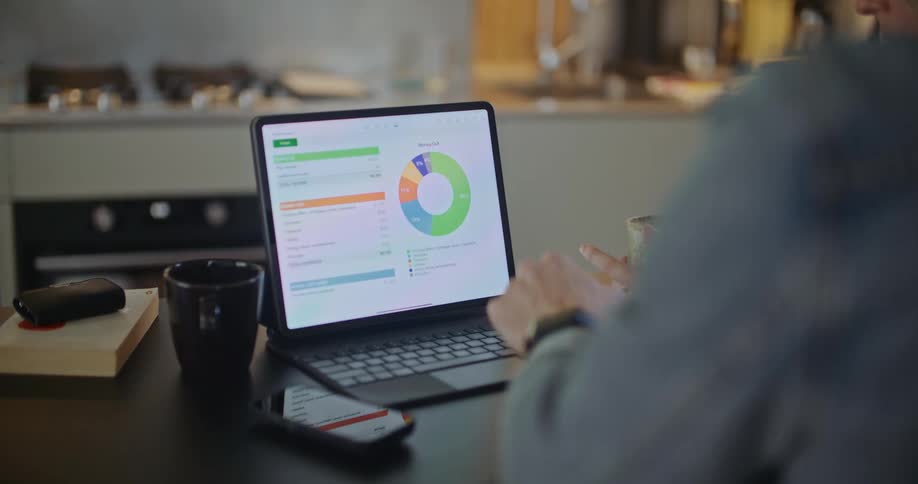 A man and a woman are sitting at a table looking at a laptop computer as he points to a chart on the screen