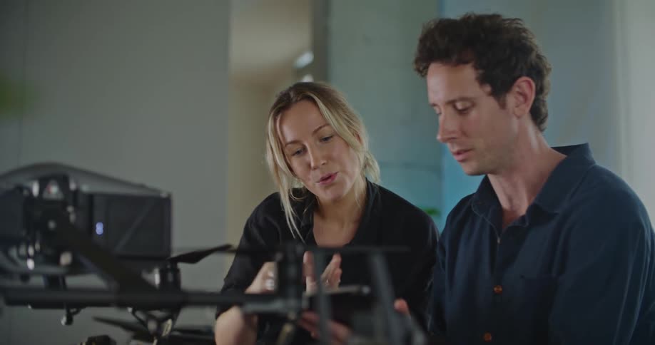 A man and woman sitting together talking looking at a tablet with a large piece of equipment in front of them