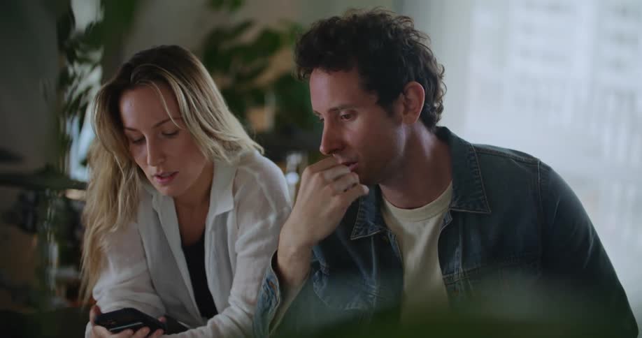 Two people are talking to each other and using a cell phone