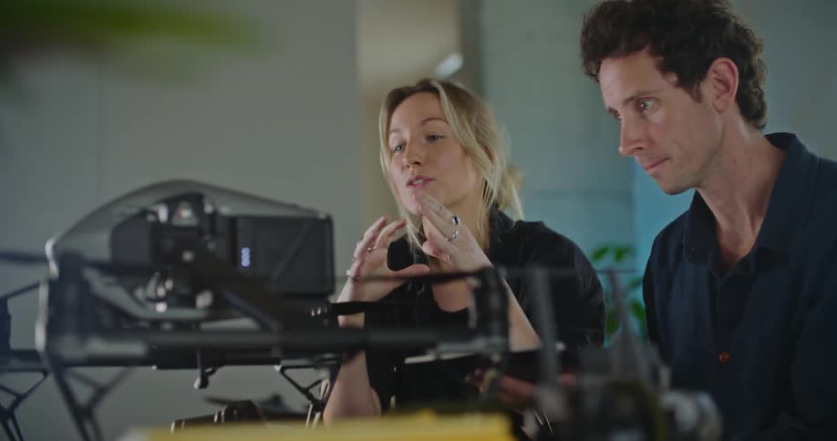 A woman talks to a man as they look at an aerial drone on a table