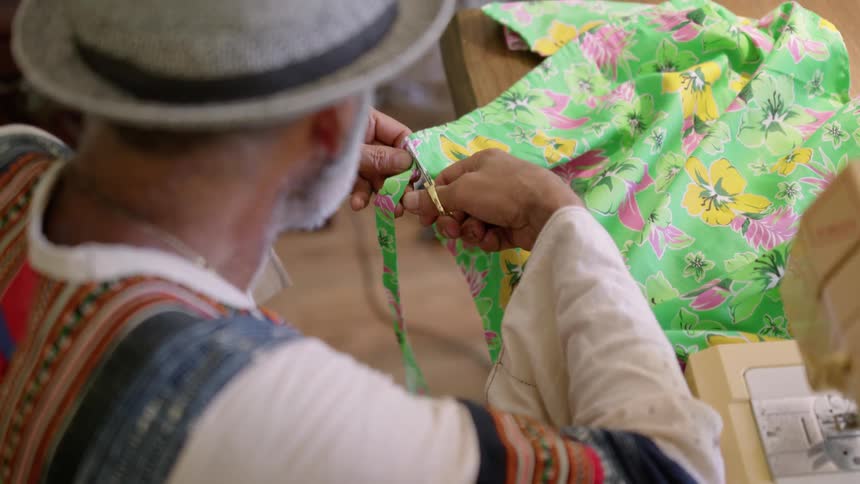 An older elderly man is sewing clothes in the middle of the day