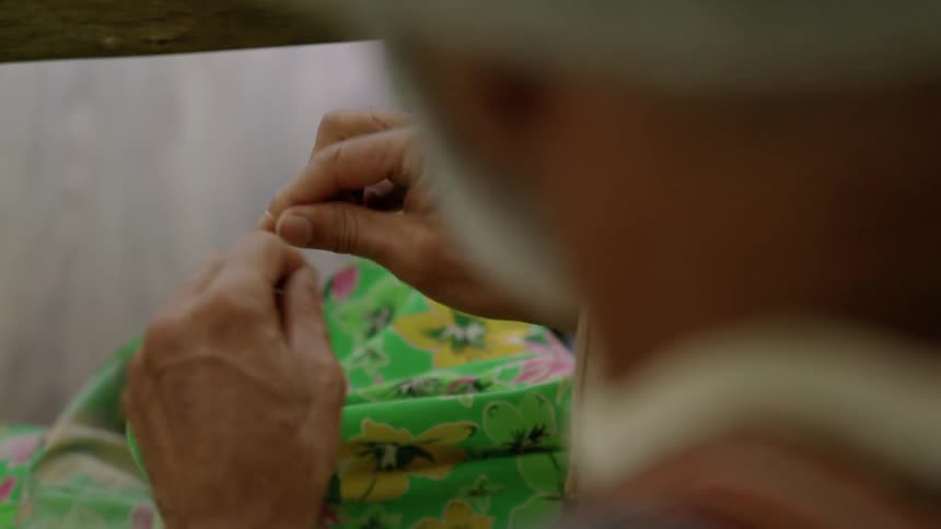 Man manipulates thread while sitting in front of colorful pile of fabric