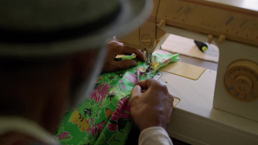 The view is of an older man that is sewing some clothes