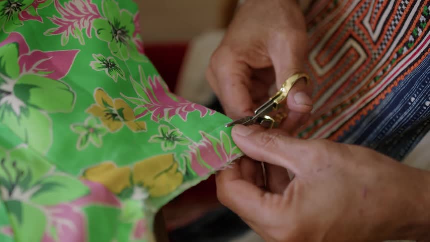 A man uses scissors to trim a piece of hawaiian print fabric