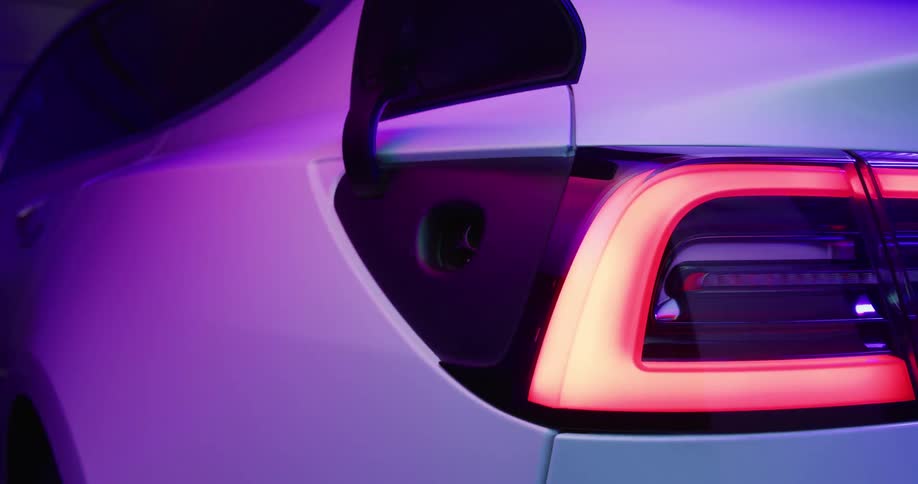 The charge flap on the back of a white electric vehicle pops open as the camera zooms in on the charging socket