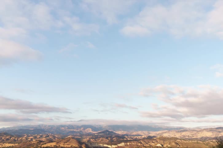 An aerial of the top peaks of mountain ranges with clouds rolling over the peaks