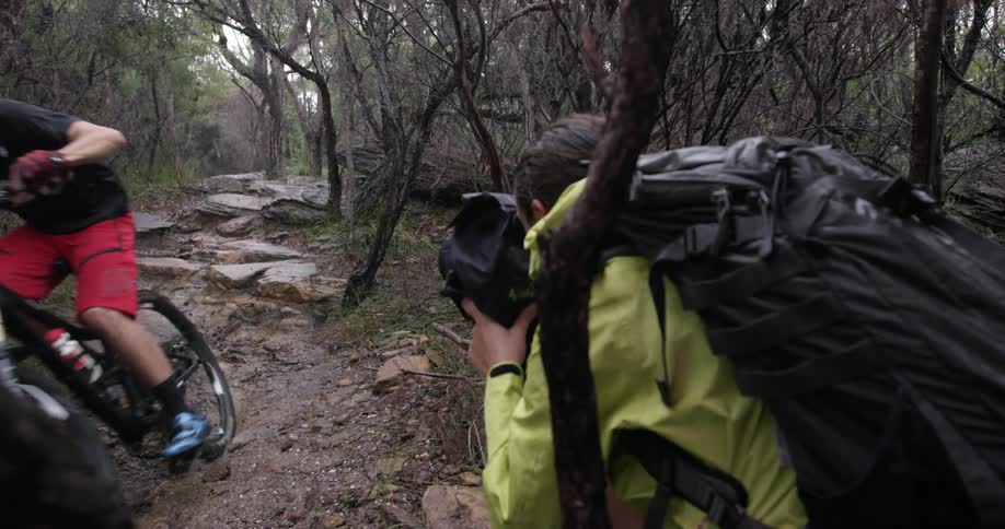 Person films another person riding a bike on a rocky path in the woods