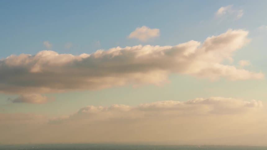 The sun shines on cumulus clouds as they move across a blue sky