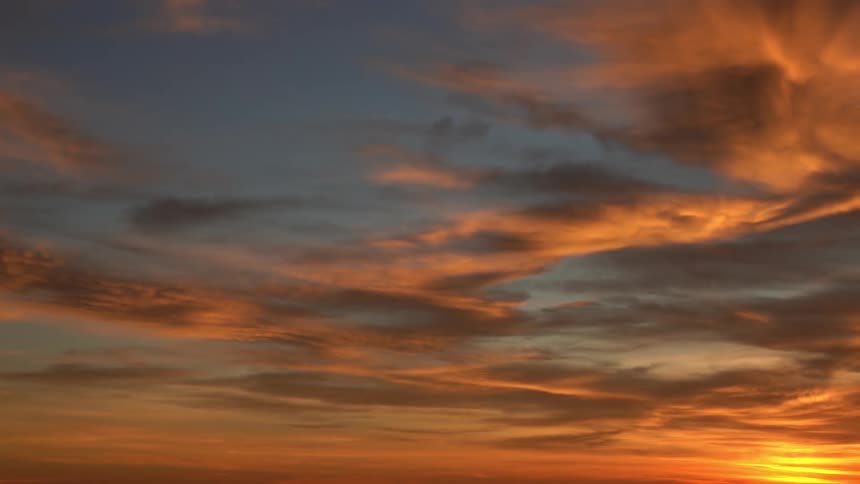 The sun shines brightly on the horizon reflecting red colors on the clouds as they move across the sky at sunset