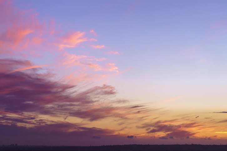 Clouds pass over a grassland at sunset