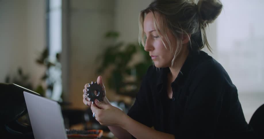 A woman sitting at her desk in front of a laptop looking at parts in her hand