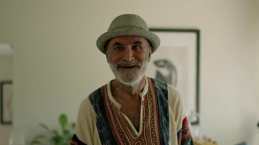 An older elderly man is smiling and talking inside of his home