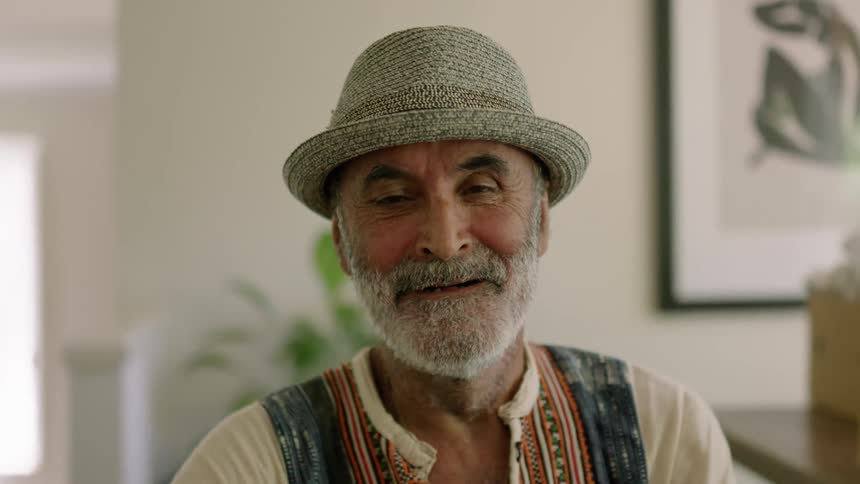 An older man is indoors and putting his hat on