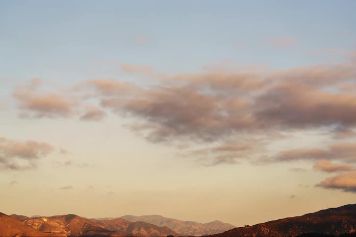 The sun shines on a mountain range as cumulus clouds move across the sky