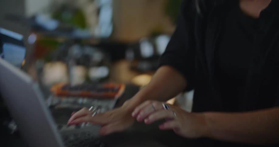 Woman talks on phone while typing on laptop at desk with machine part nearby