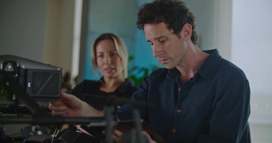 Coworkers talk in office while one uses tablet to adjust machine