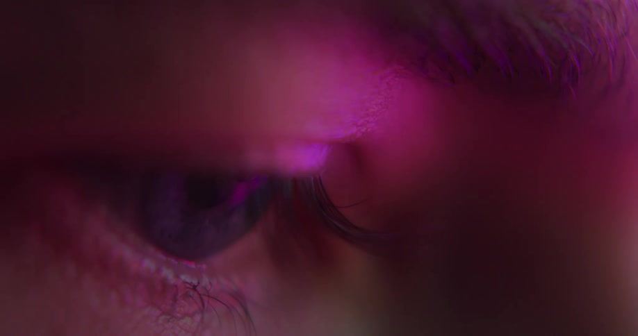 Colored light shines on a persons eye as they blink and look around