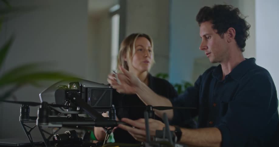 A man and a woman are standing in a room as he turns a drone around and sets it on the table