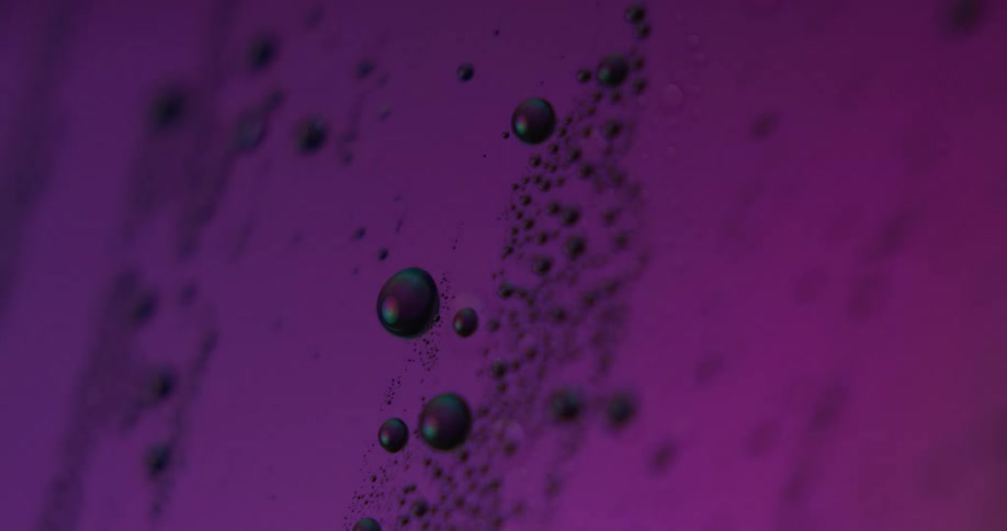 Abstract droplets of inklike liquid float under rainbow neon lights