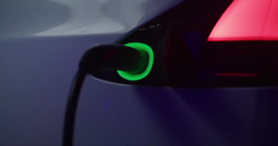 Electric vehicle plugged into wall while green light flashes as it chargers