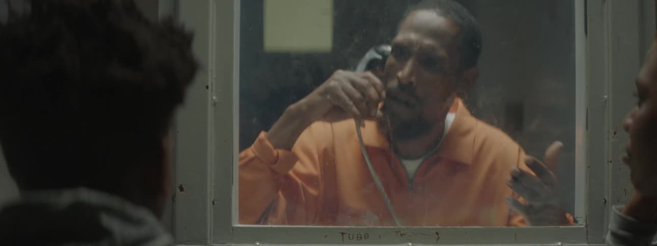 A man talks through a prison phone at a boy