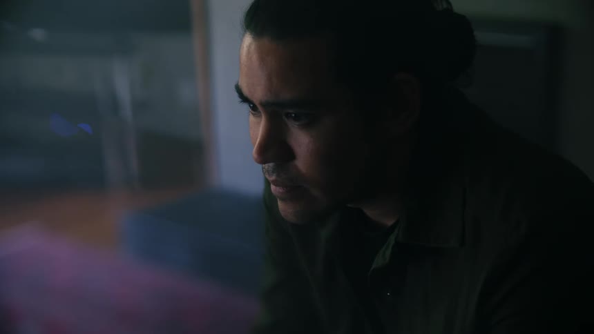 A man sitting down in a black shirt looking ahead of him contemplatively