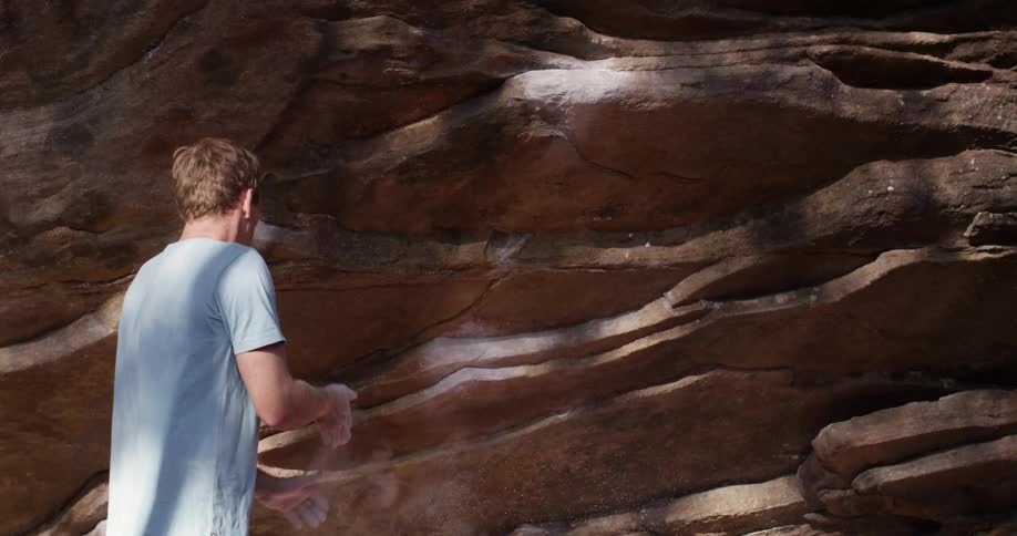 A man brushes dirt off his hands next to a rock formation