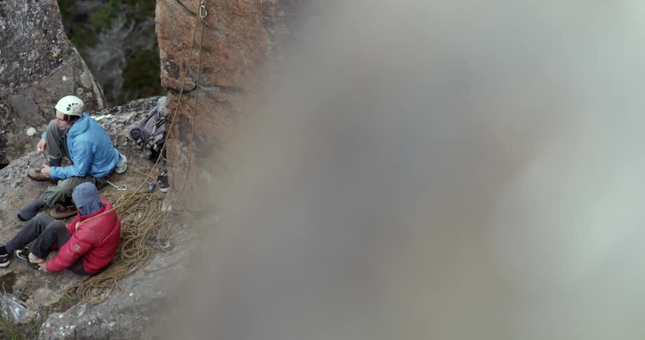 Two people sit at the bottom on a rocky cliff