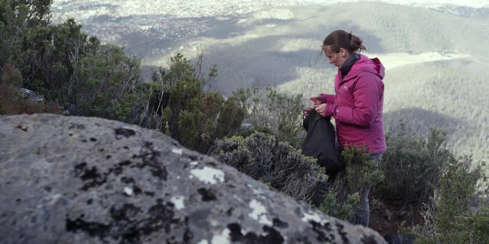 A woman puts rope in her backpack on the side of a mountain