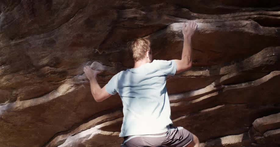 A man is rock climbing on a sunny day