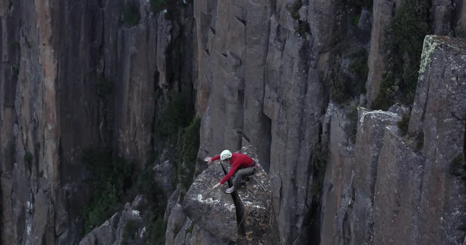 Person jumps down a steep cliff and lands onto a rock