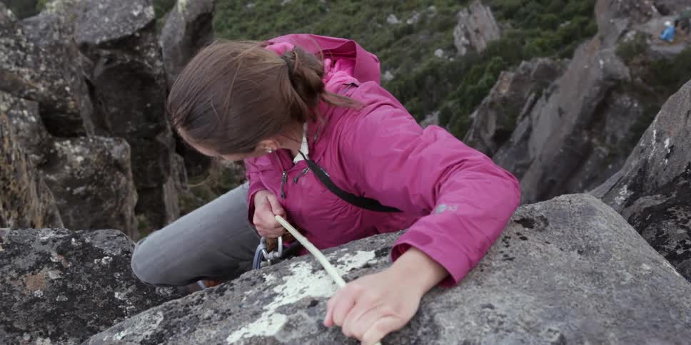 A woman using a rope climbs up a steep cliff
