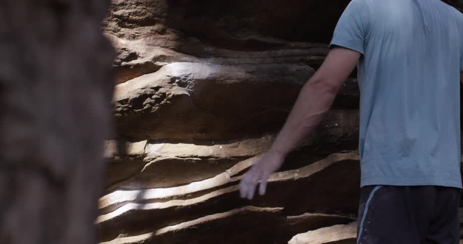 A man waves his arms back and forth next to a large rock formation