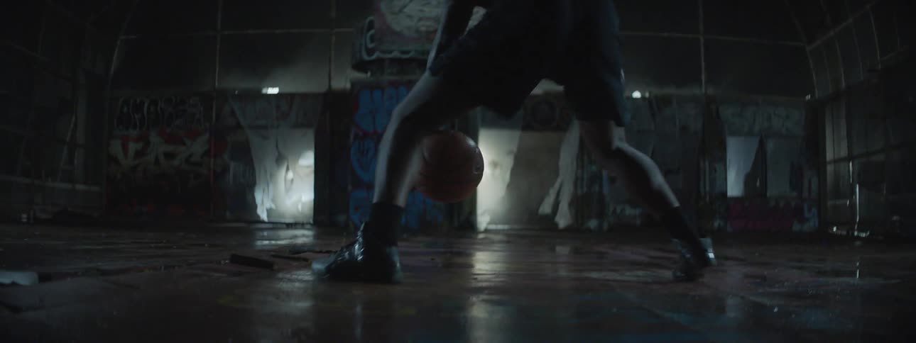 A man is dribbling a basketball on a dark court