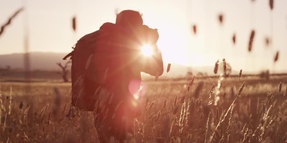 A photographer standing in a field raises her camera to her eyes